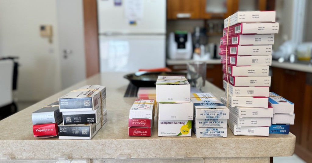 Rubber-banded medication boxes lined up in a row on a kitchen counter next to a pill organizer